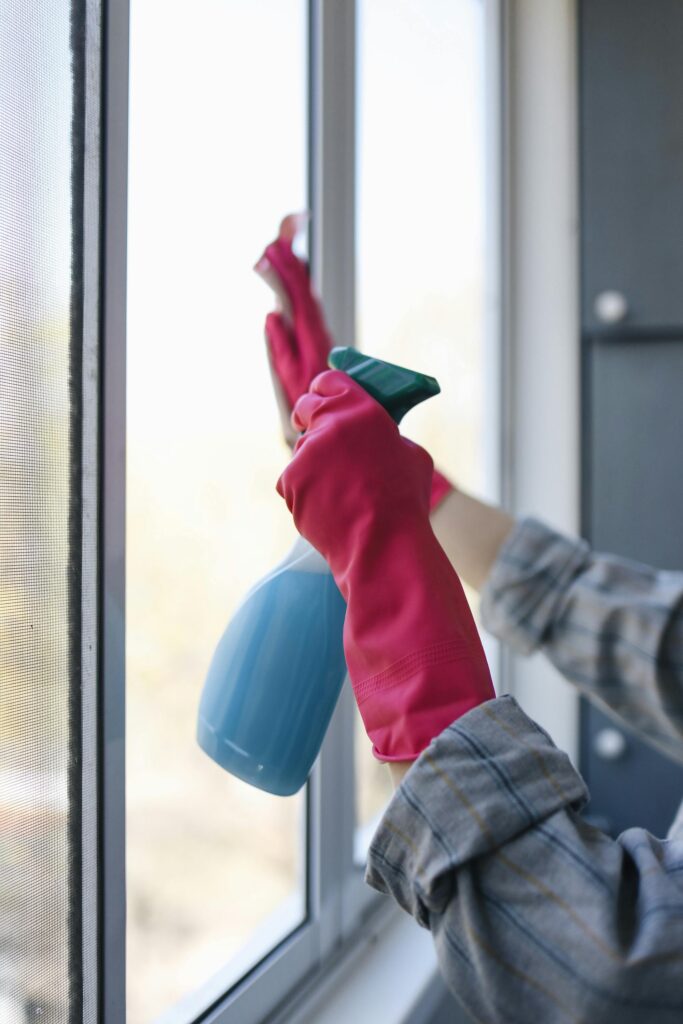 lawn-01 Hands in rubber gloves using a spray bottle to clean a window indoors.