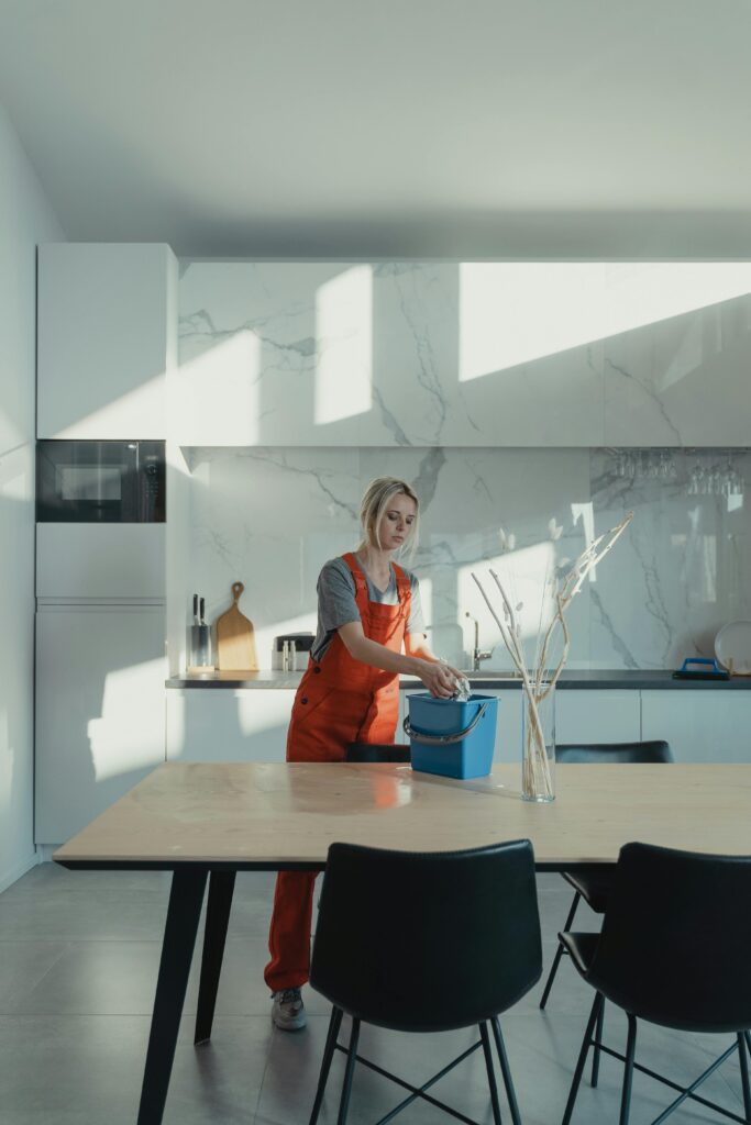 Residential Cleaning A woman in uniform cleaning a modern kitchen lit by natural light, creating a serene atmosphere.